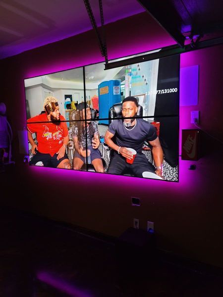 Large video display showing people, with purple LED backlighting on a dark wall.