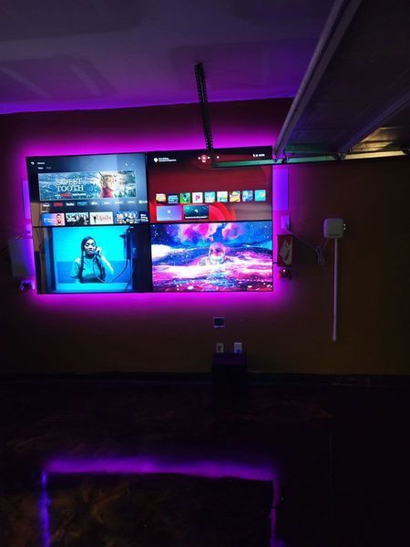 Purple-lit media wall with multiple screens displaying streaming services and a bottom-lit floor in a dark room.