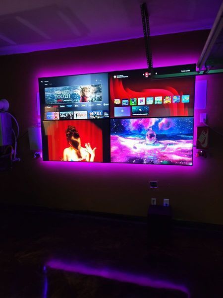 Wall-mounted screens displaying various content, illuminated with purple LED strips.
