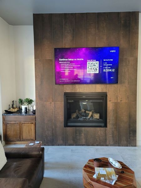 TV screen over fireplace on a brown wooden accent wall; a coffee table in the foreground.
