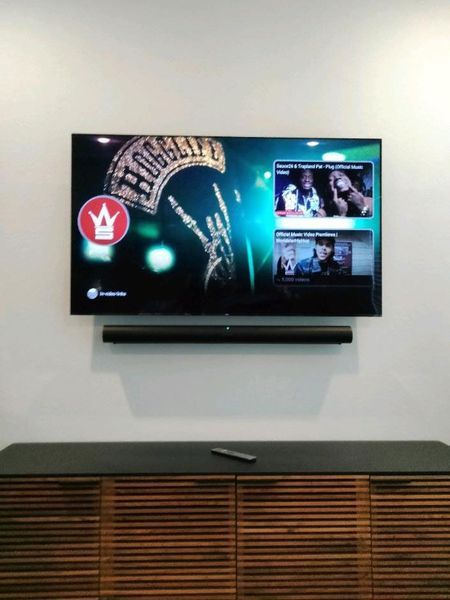 TV mounted on a wall with soundbar below, and a cabinet below the soundbar. The TV shows a streaming service and is tuned to a rock channel.