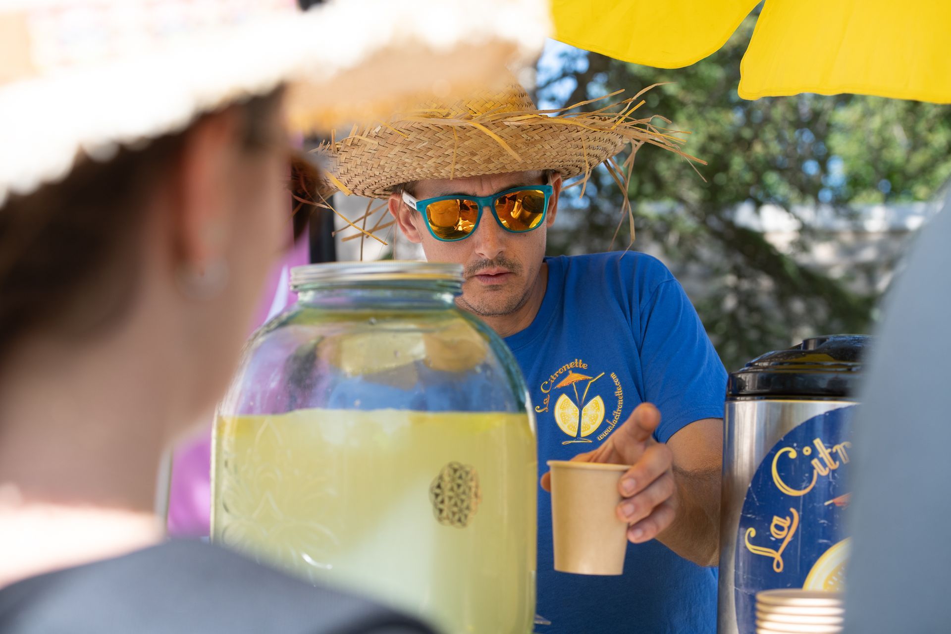 Un homme portant un chapeau de paille et des lunettes de soleil sert une boisson à une femme.