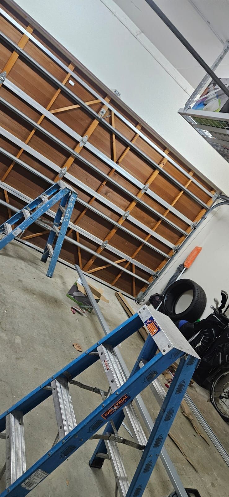 A blue ladder is sitting in a garage next to a garage door.