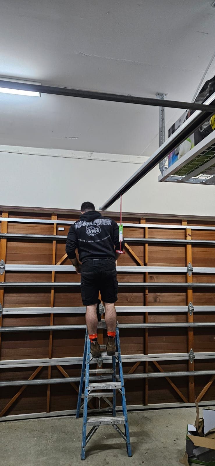 A man is standing on a ladder working on a garage door.