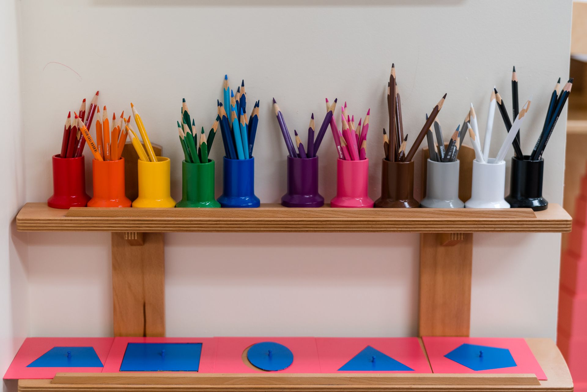 A shelf with montessori colored pencils and metal insets.