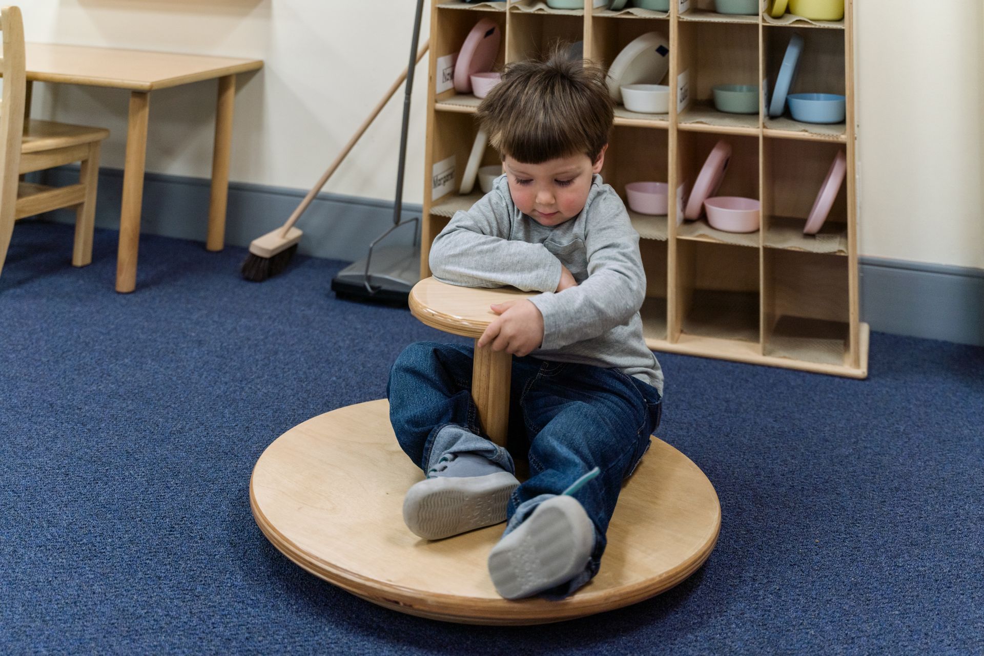 A montessori child is sitting on a wooden balance board.