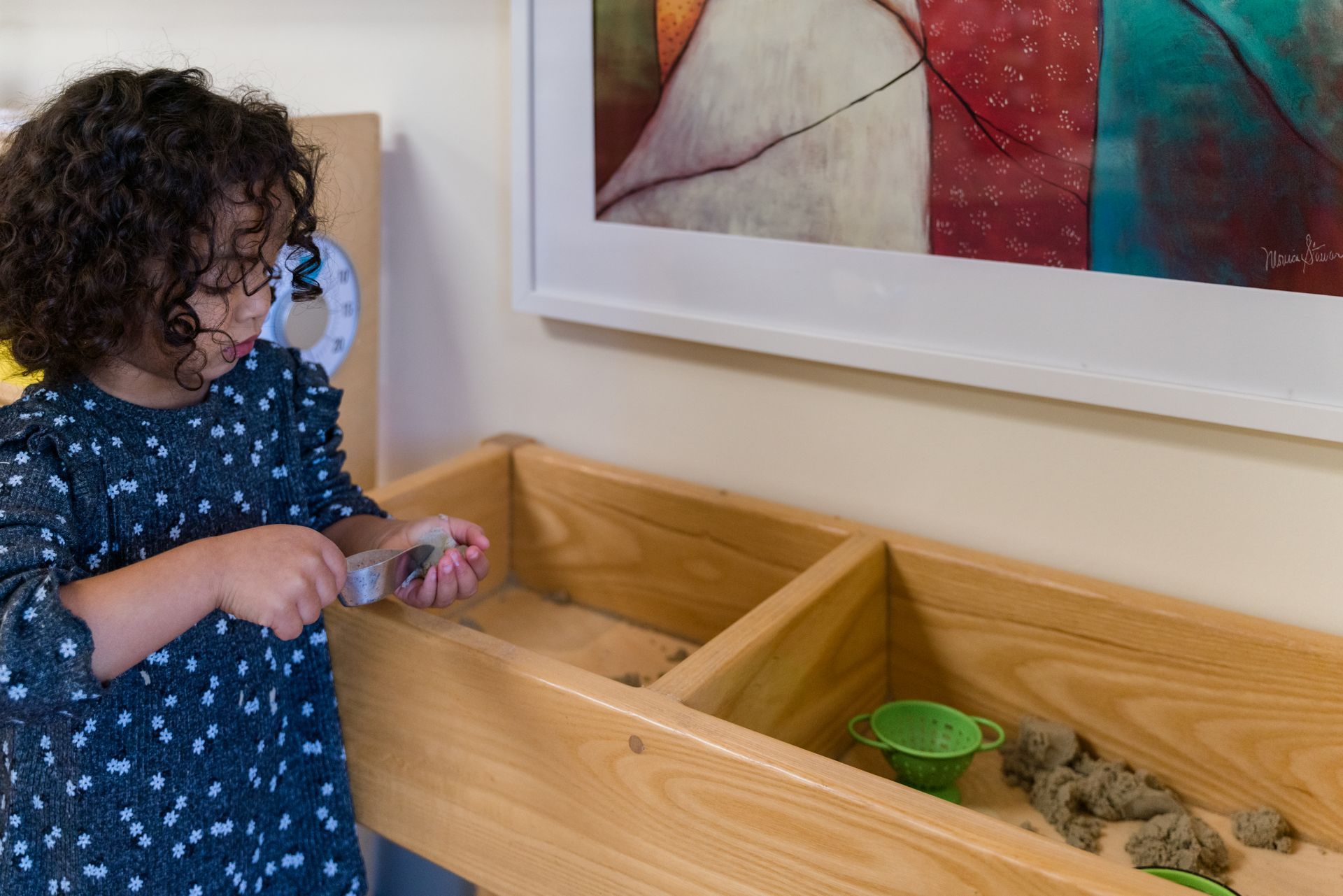 A montessori child is working with sand in a wooden box.