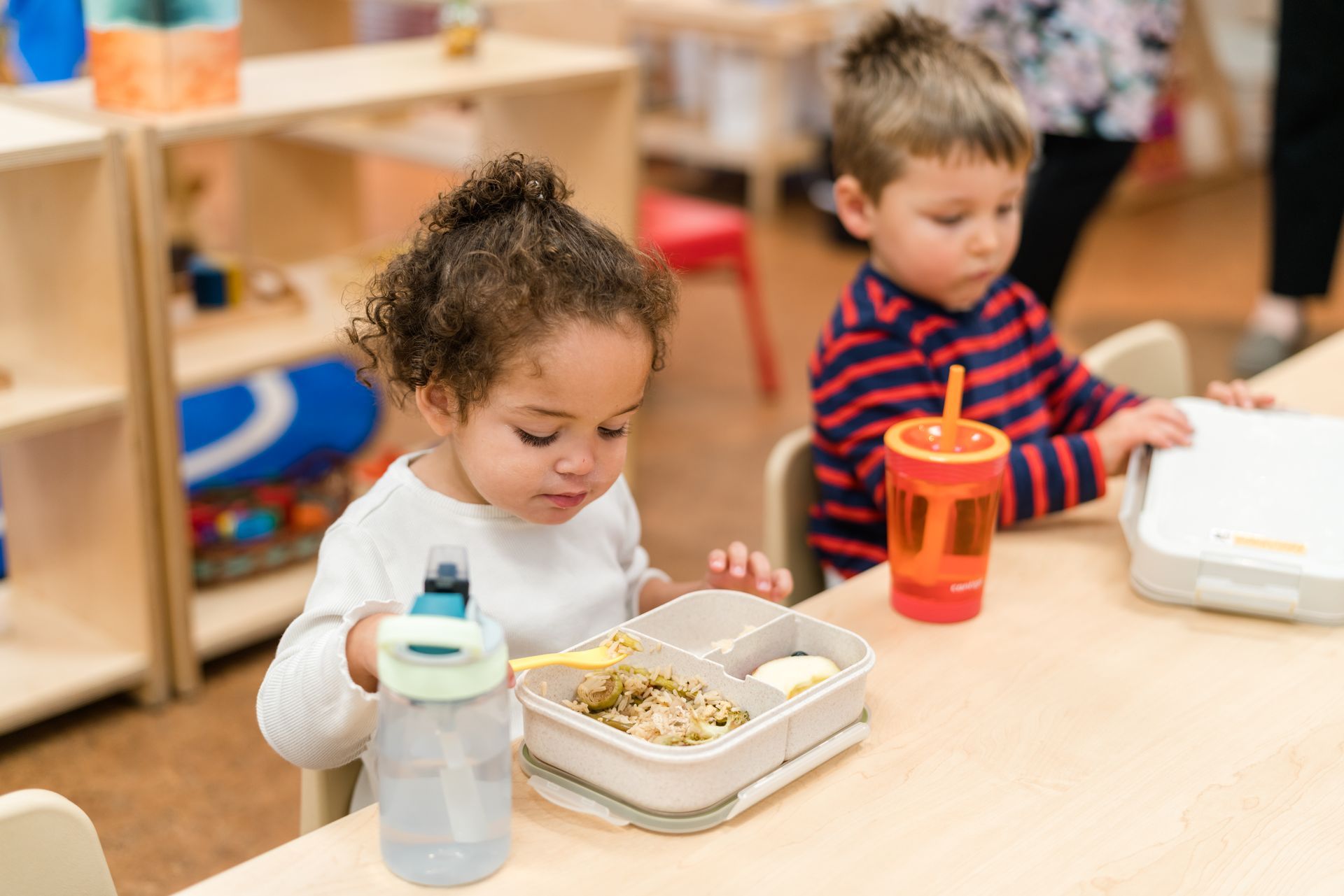 Montessori children are sitting at a table eating lunch.