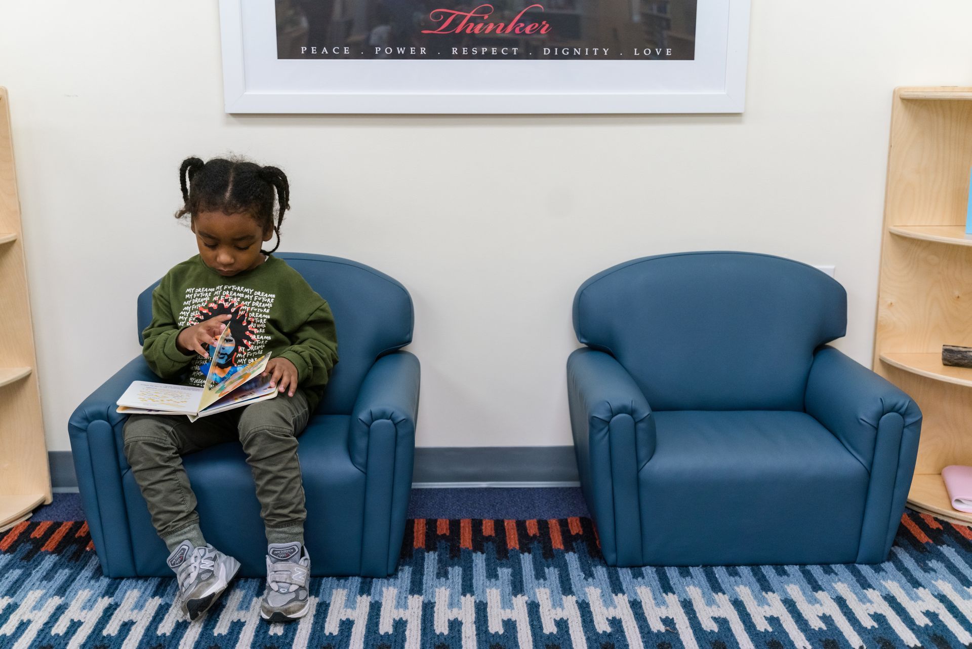 A montessori child is sitting in a chair reading a book.