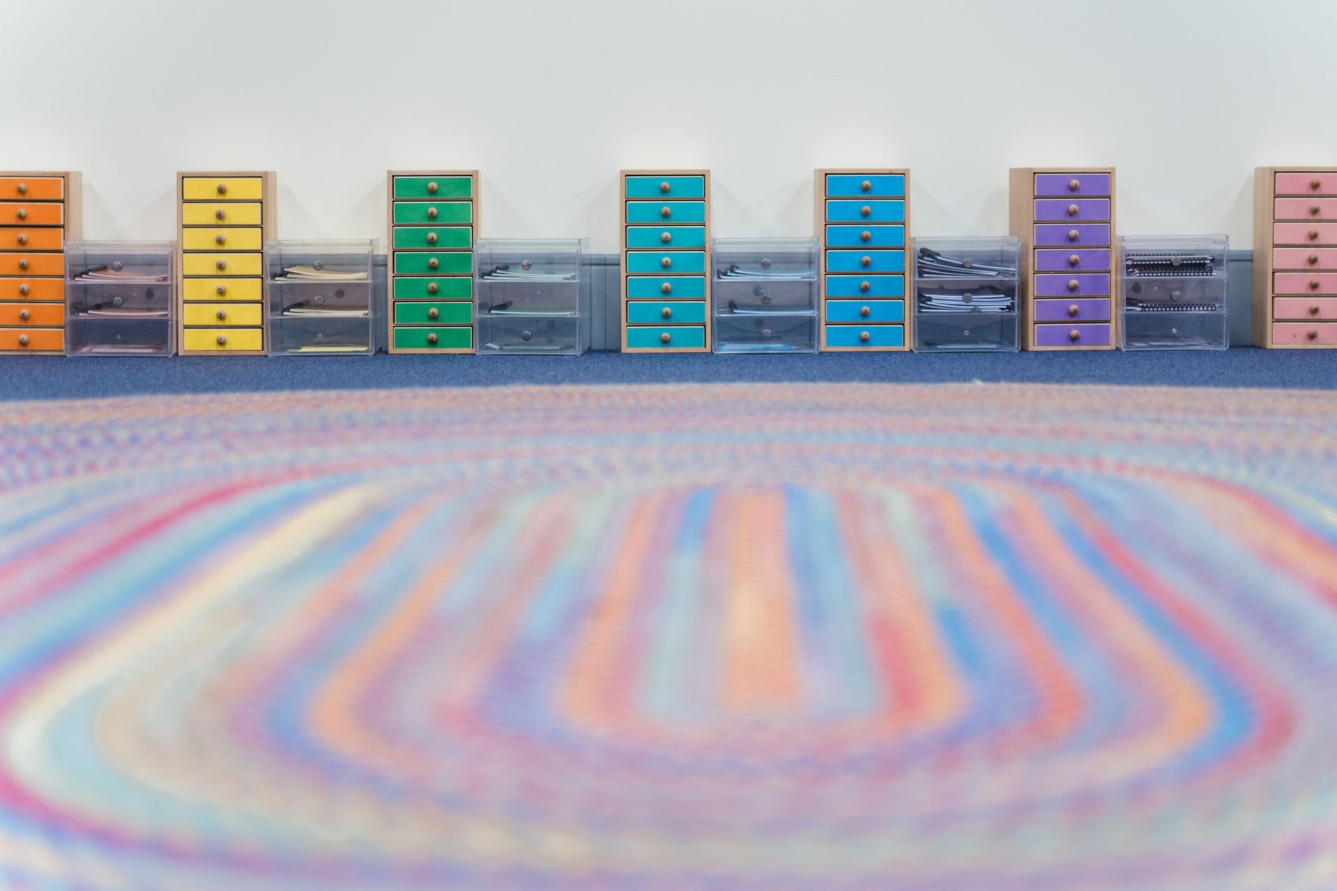 A montessori classroom with a rainbow rug and a row of colorful drawers.