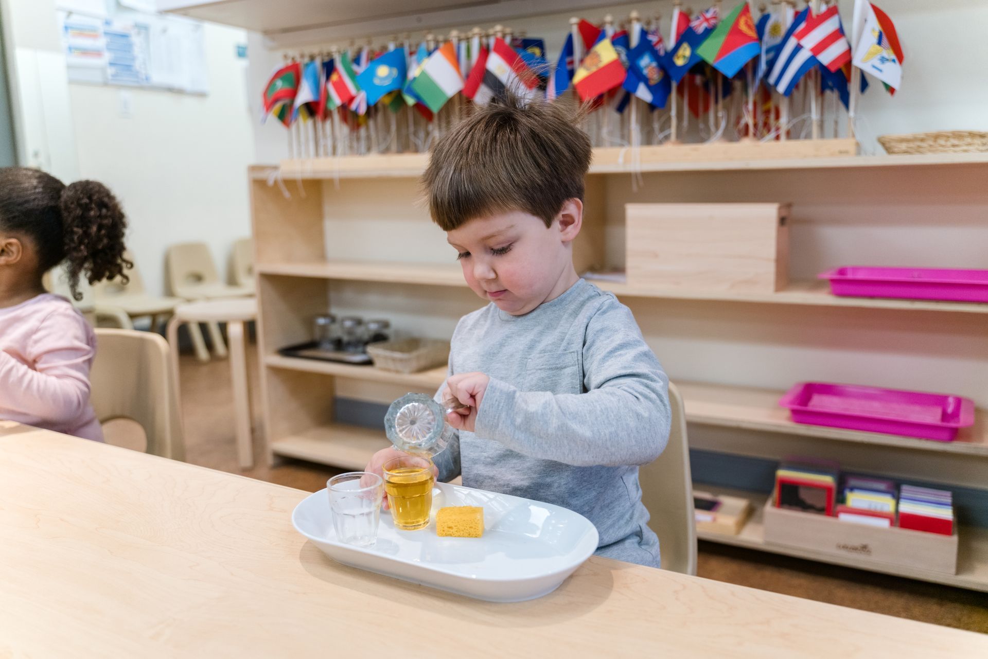A montessori child is sitting at a table pouring liquid into a cup.