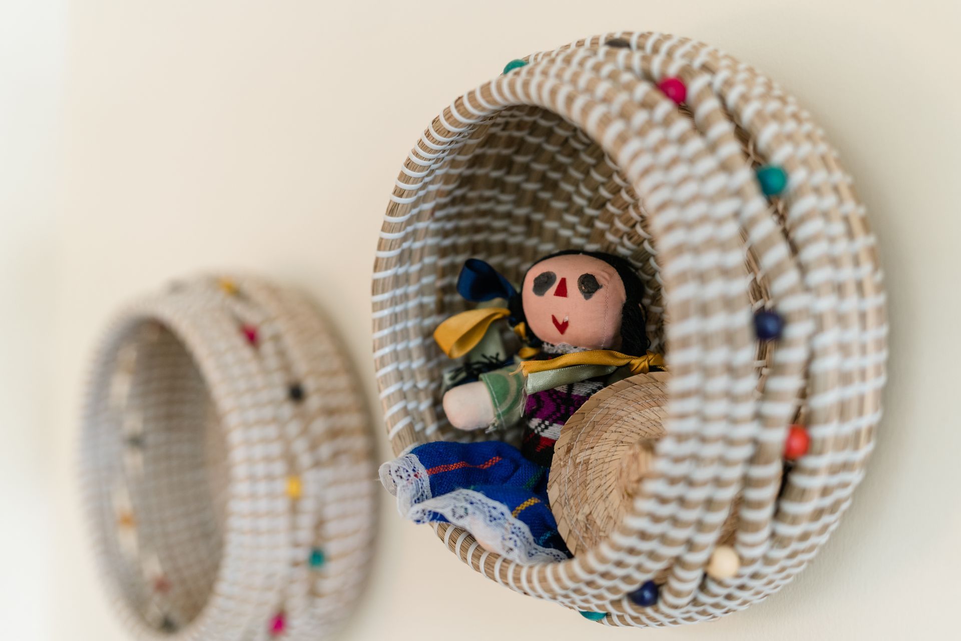 A doll is sitting in a basket next to another basket.