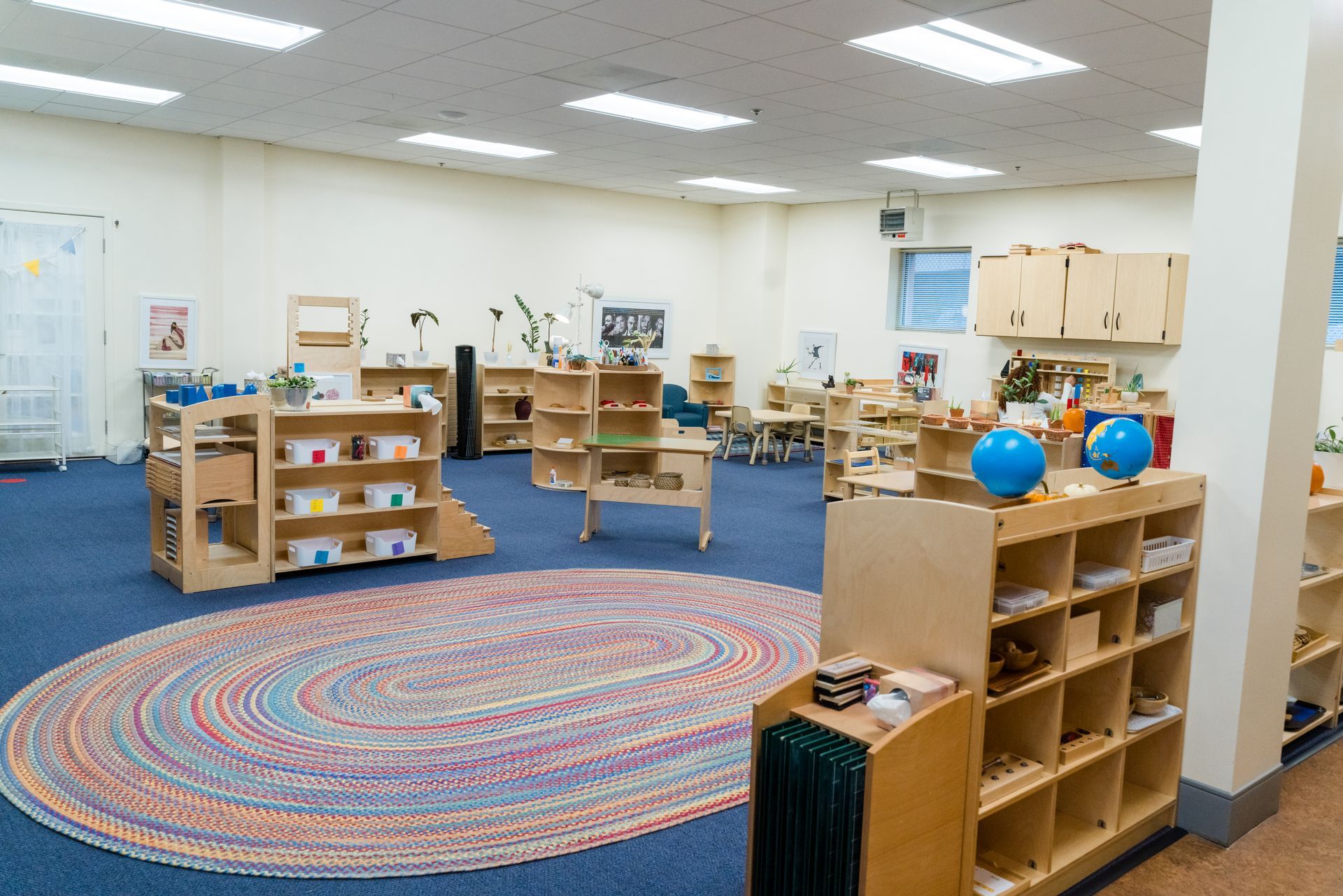 A montessori classroom with a rug, shelves, tables and a globe.
