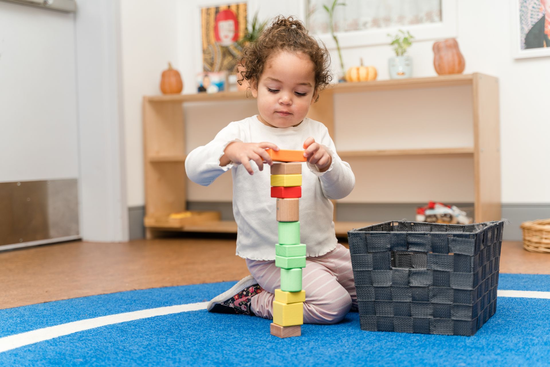 A child is sitting on the floor working with montessori wooden blocks.