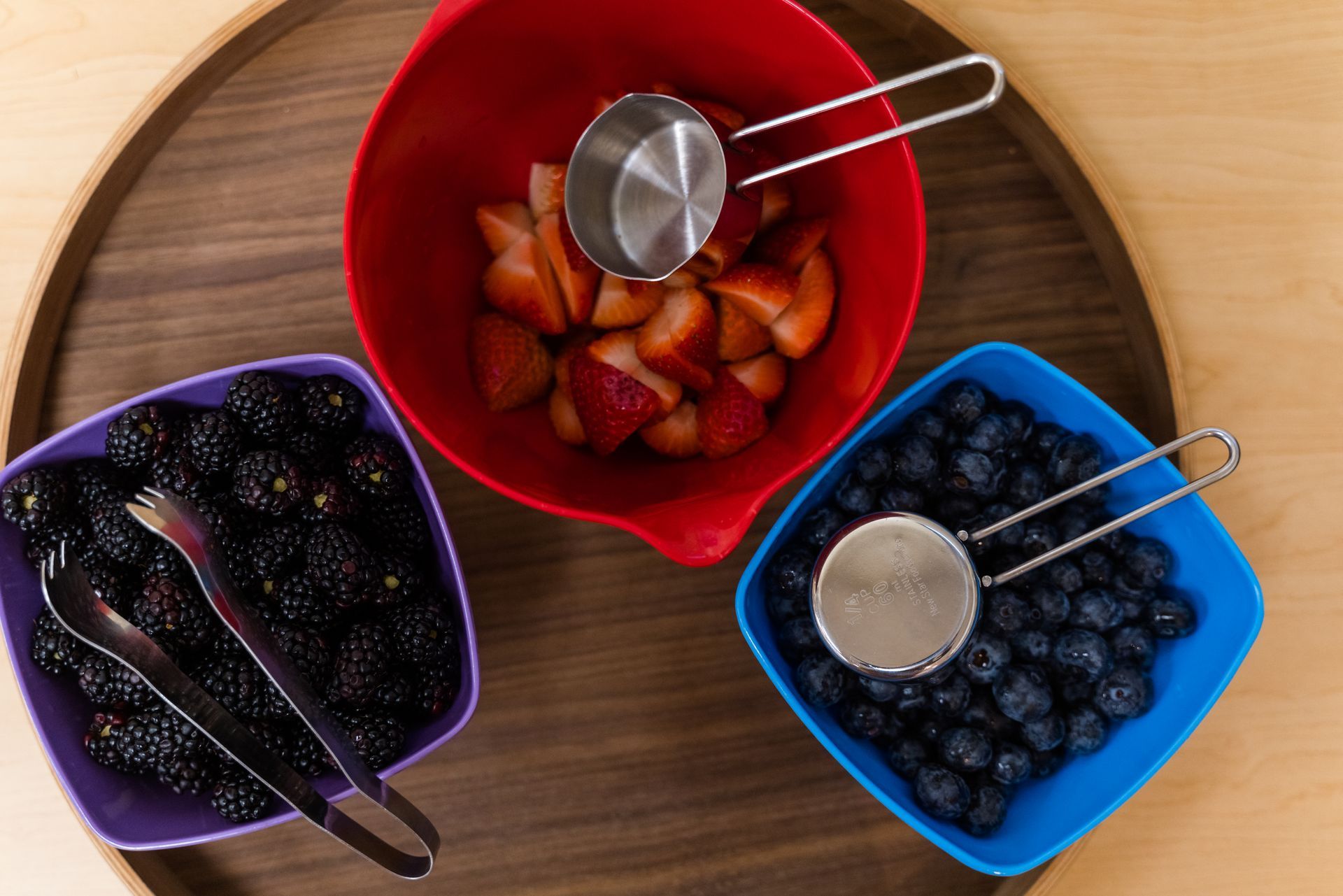 Three bowls of berries and measuring cups on a wooden tray.