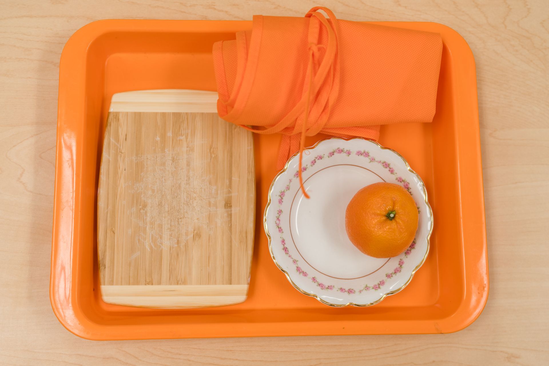 An orange tray with a plate and an orange on it.