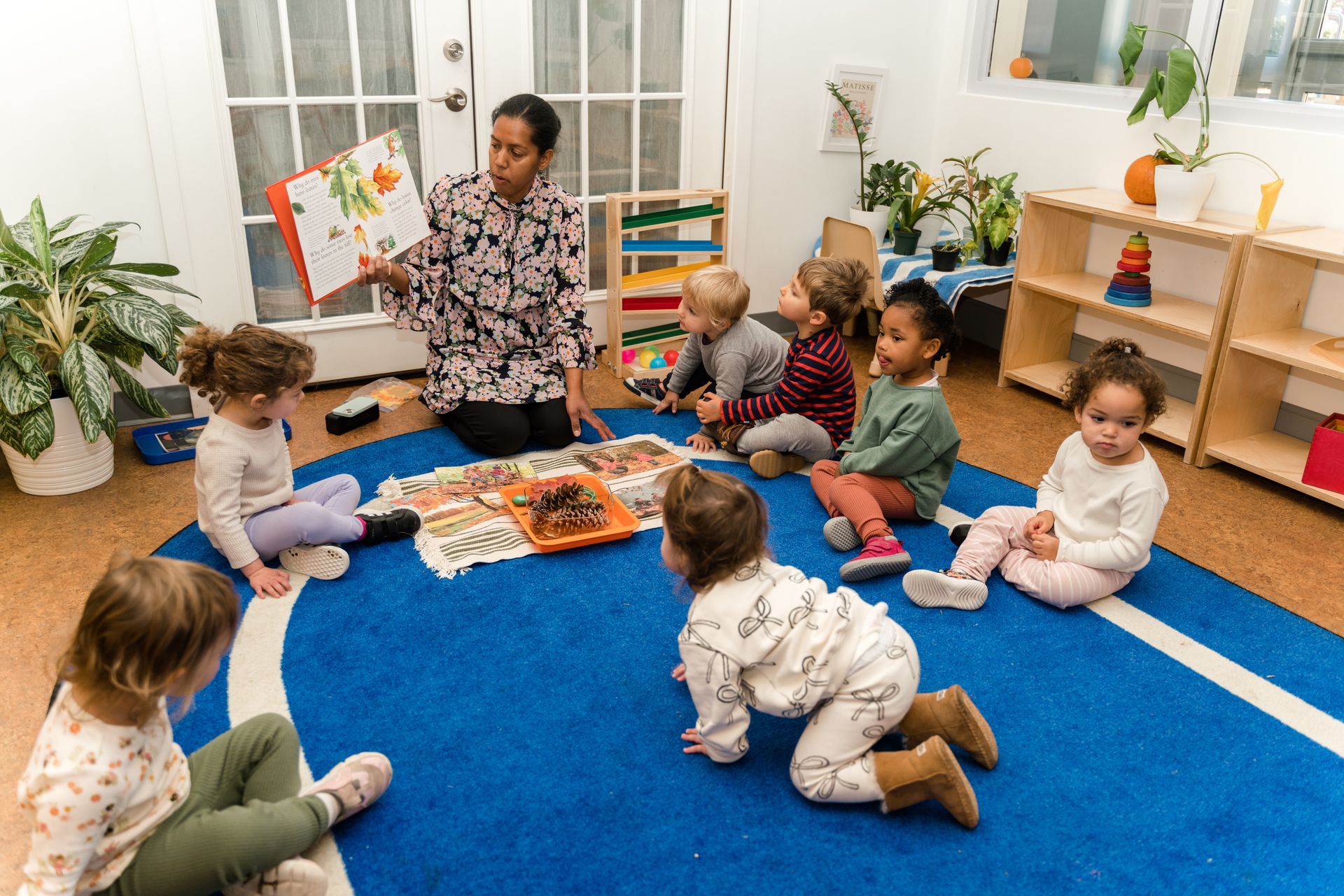 A montessori guide is reading a book to a group of children.