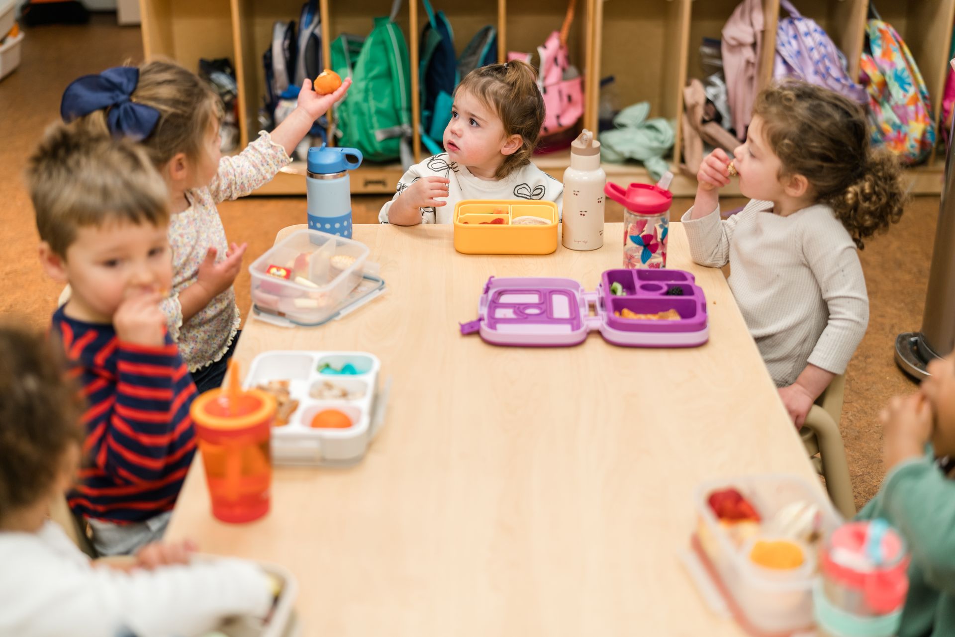 A group of montessori children are sitting at a table eating lunch.