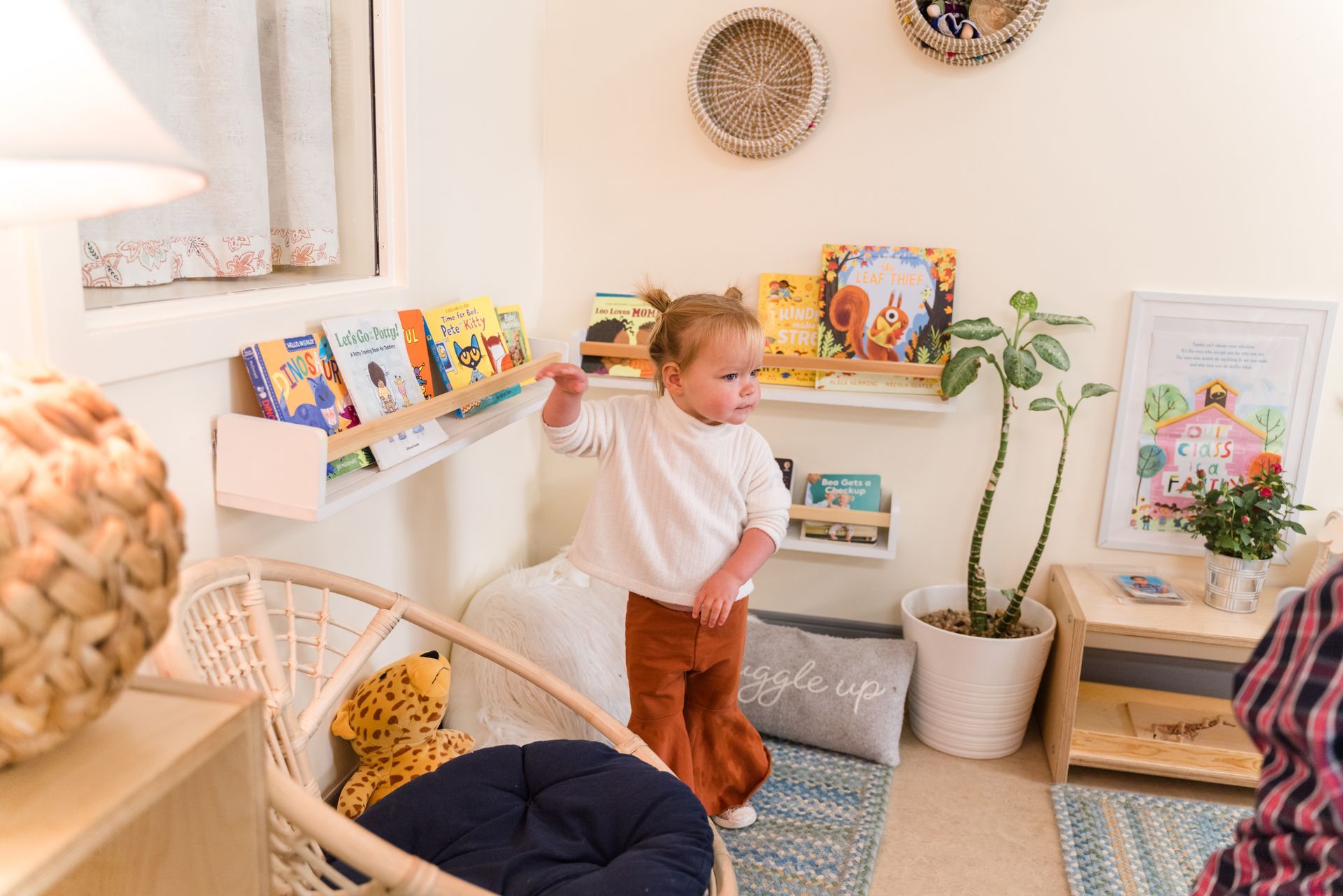 A montessori child is standing in a room next to a bookshelf.