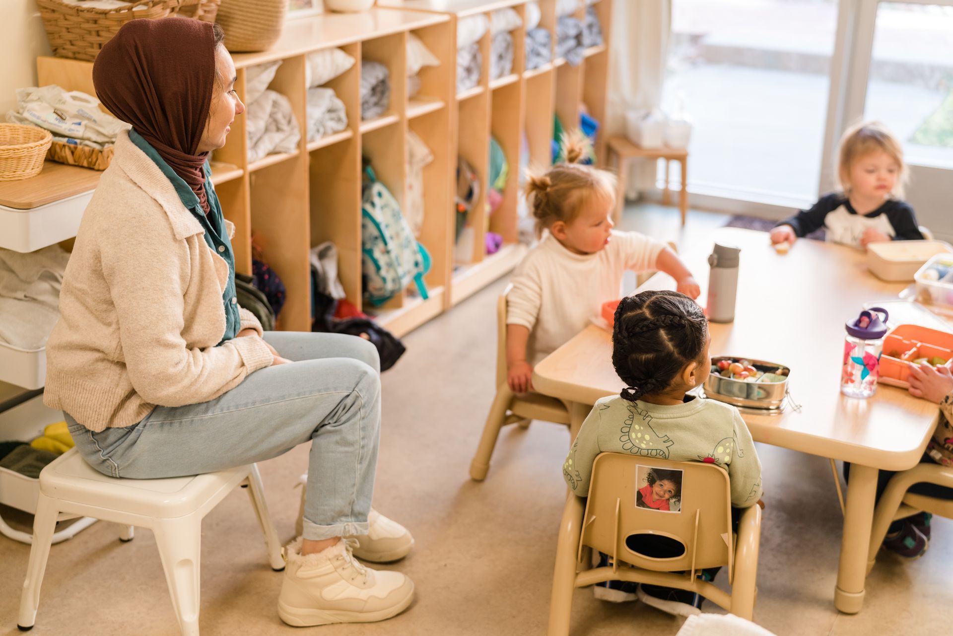 A montessori guide is sitting at a table with a group of children.