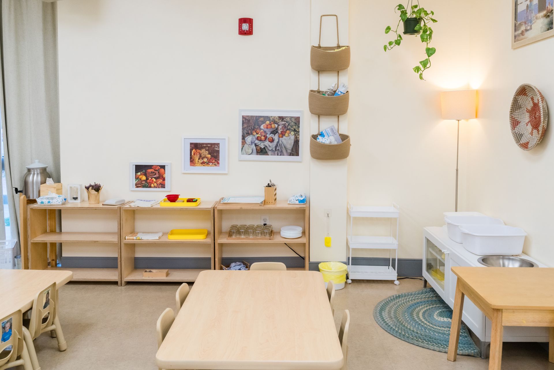 A montessori classroom with a table, chairs, shelves and a lamp.