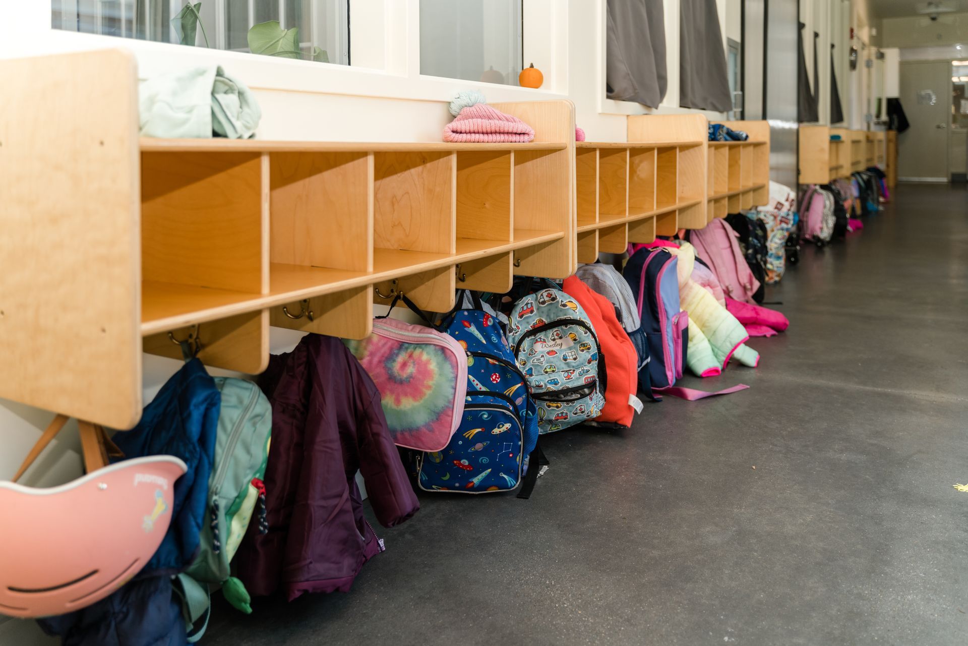 A row of backpacks and coats are lined up in a hallway.