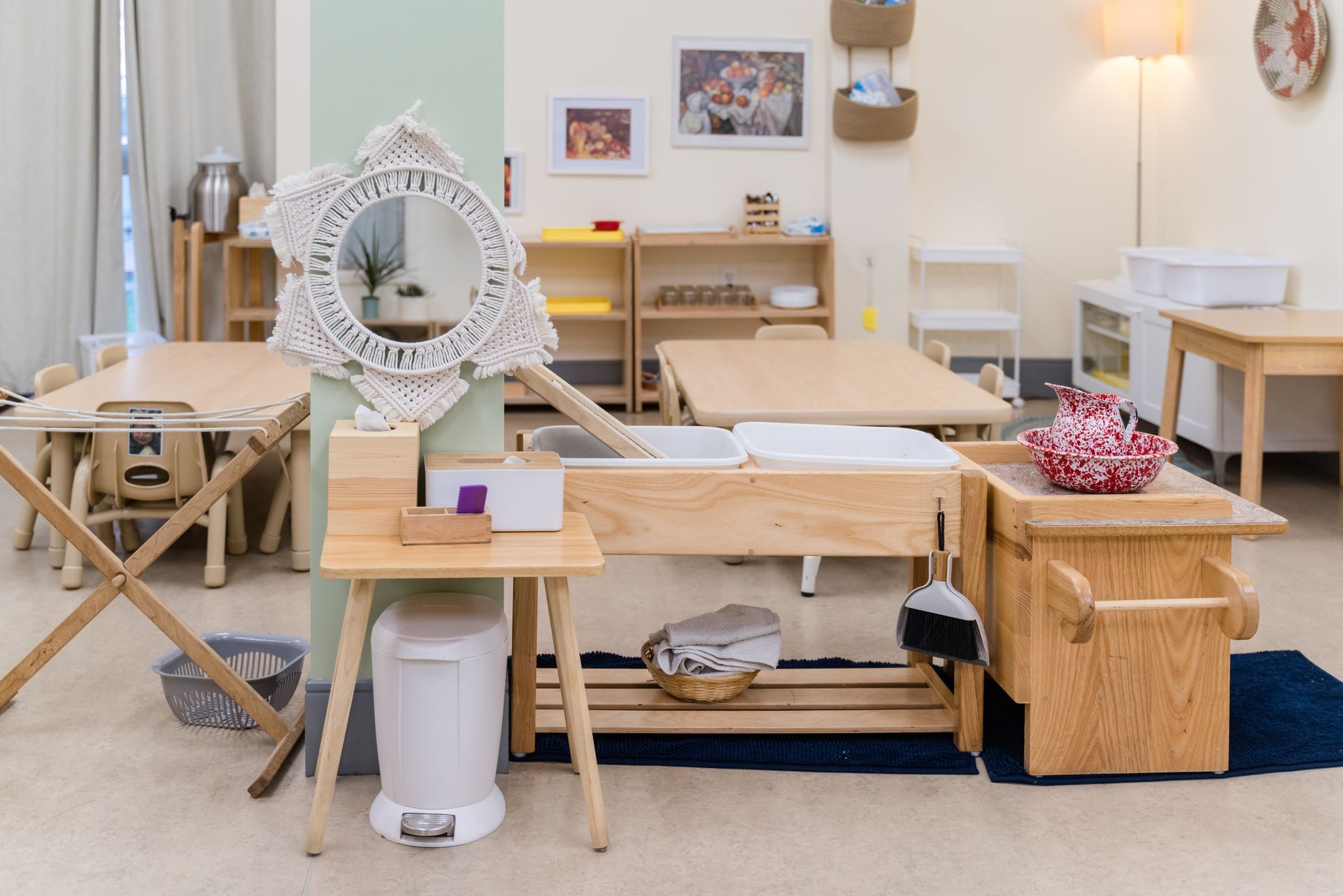 A montessori classroom with tables, chairs, a trash can and a mirror.