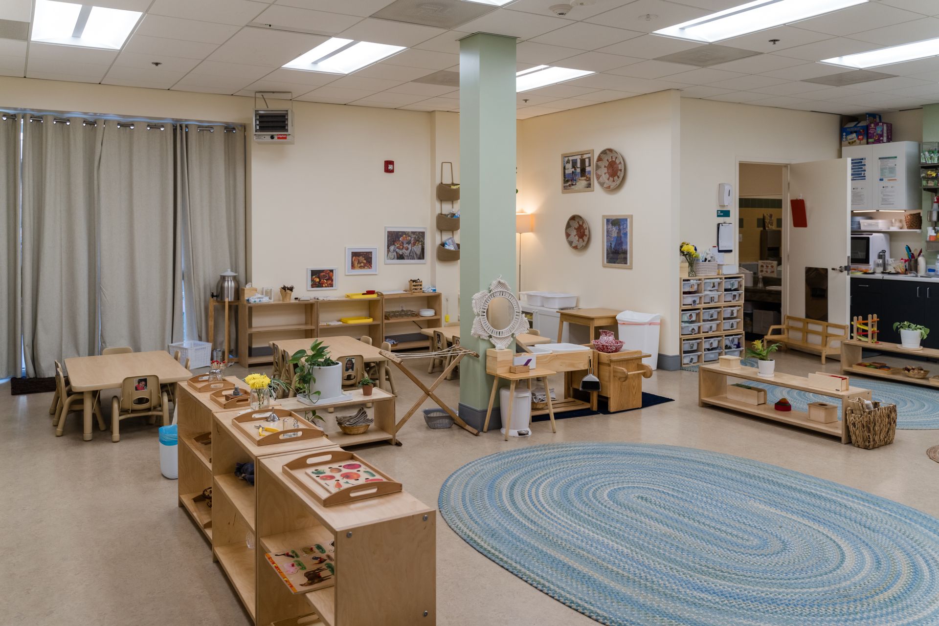 A large montessori classroom with tables and chairs and a blue rug.