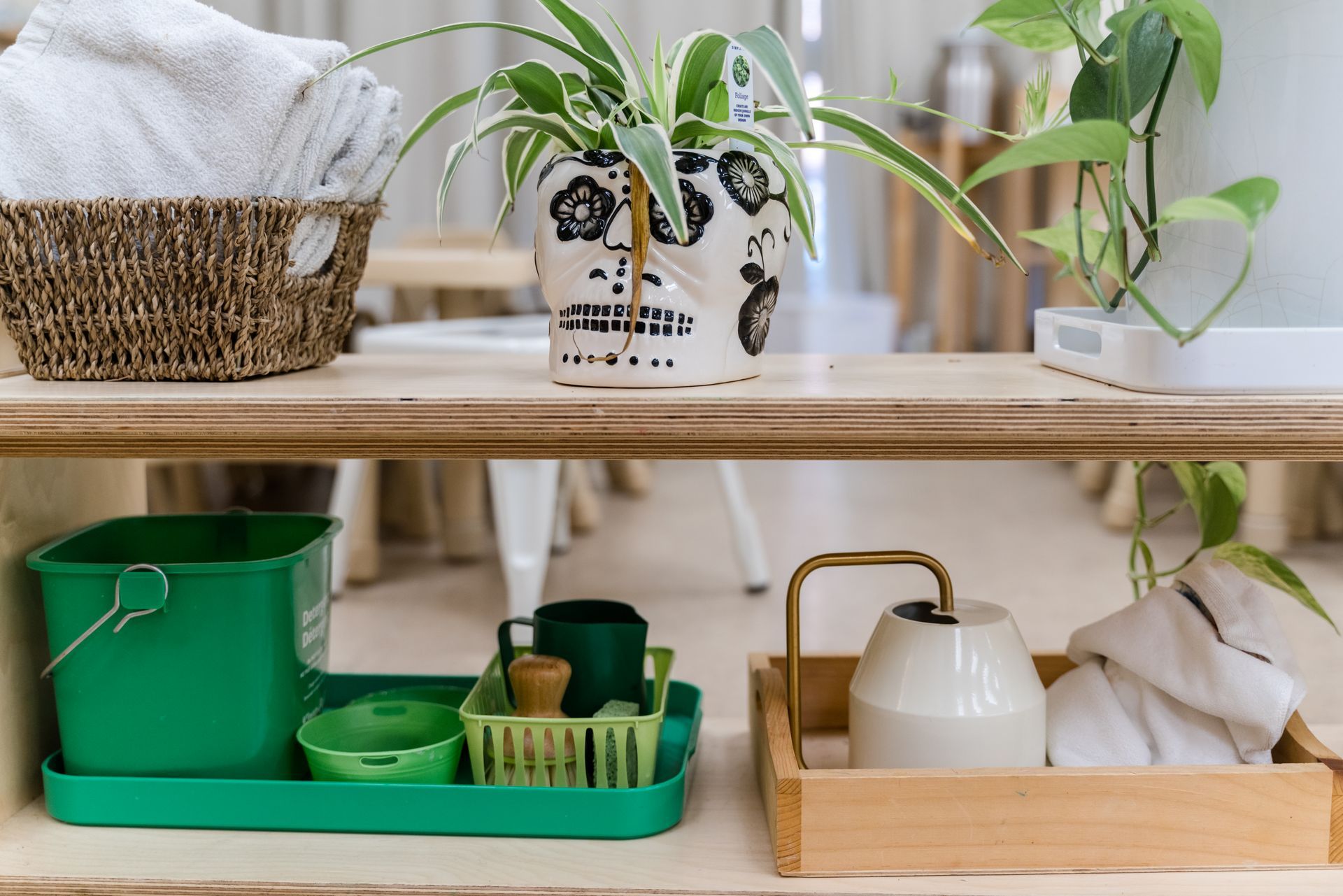 A wooden shelf with a basket, potted plants, and a watering can on it.