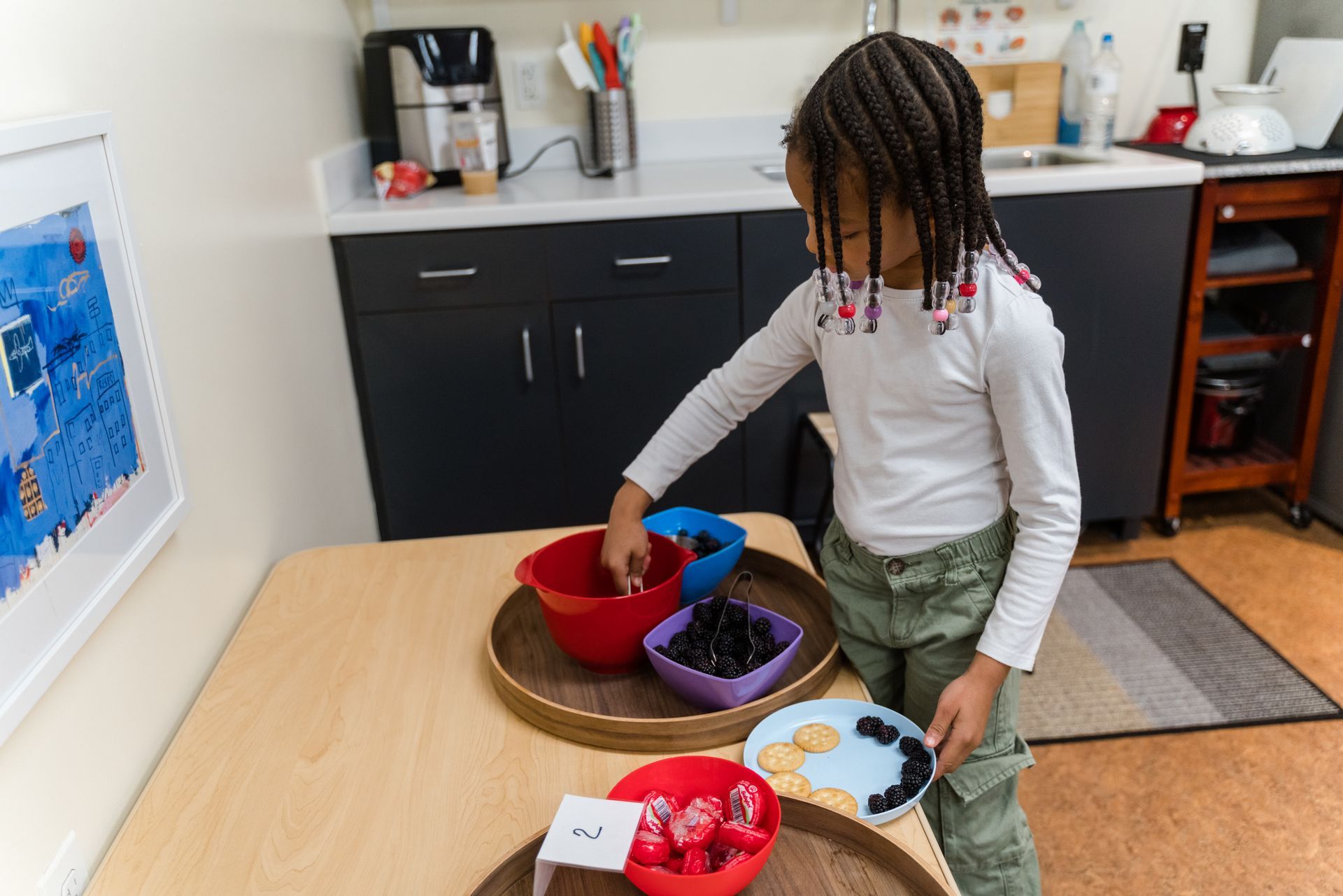 A montessori child is standing at a table with bowls of fruit on it.