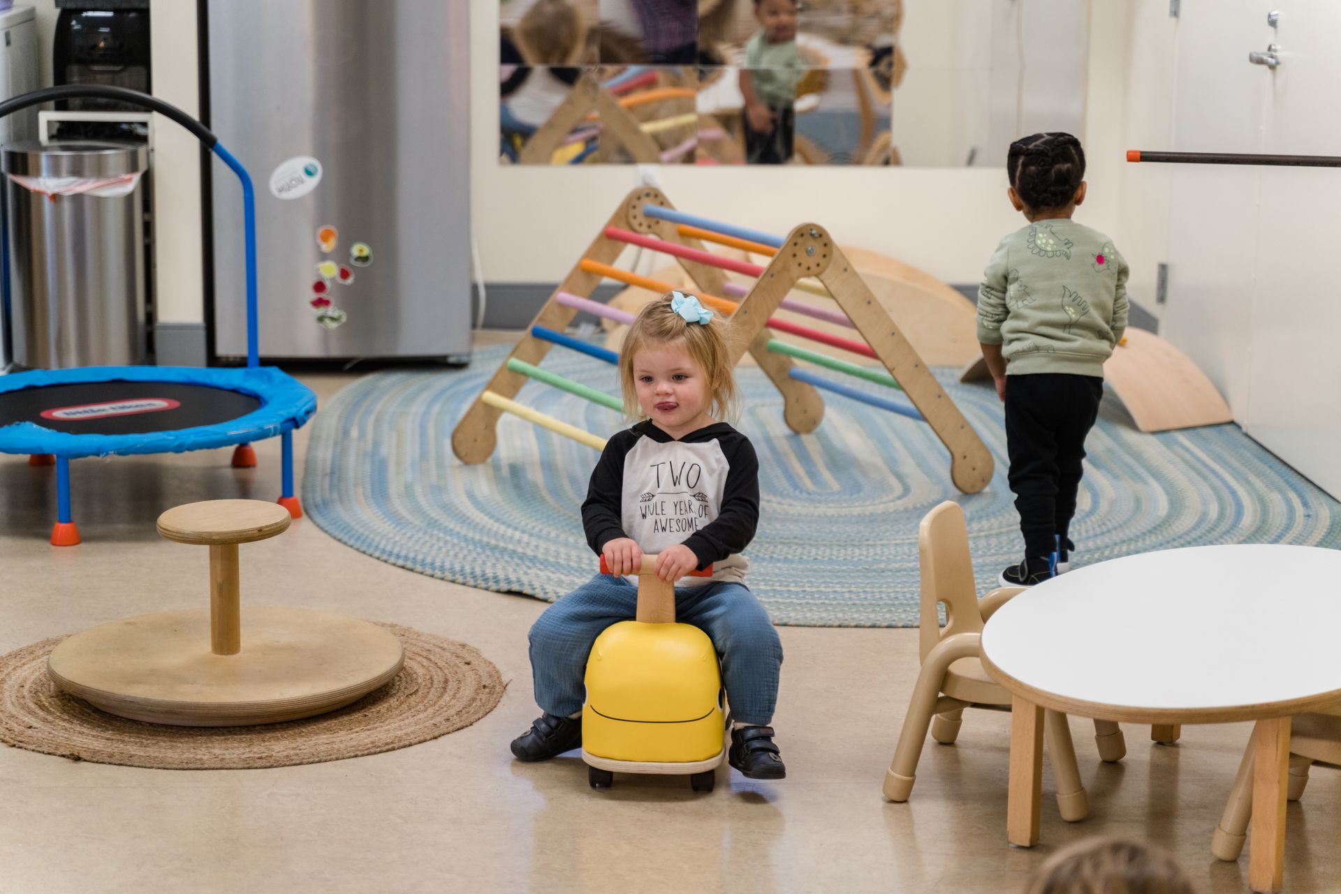 A child is sitting on a yellow montessori material in a classroom.