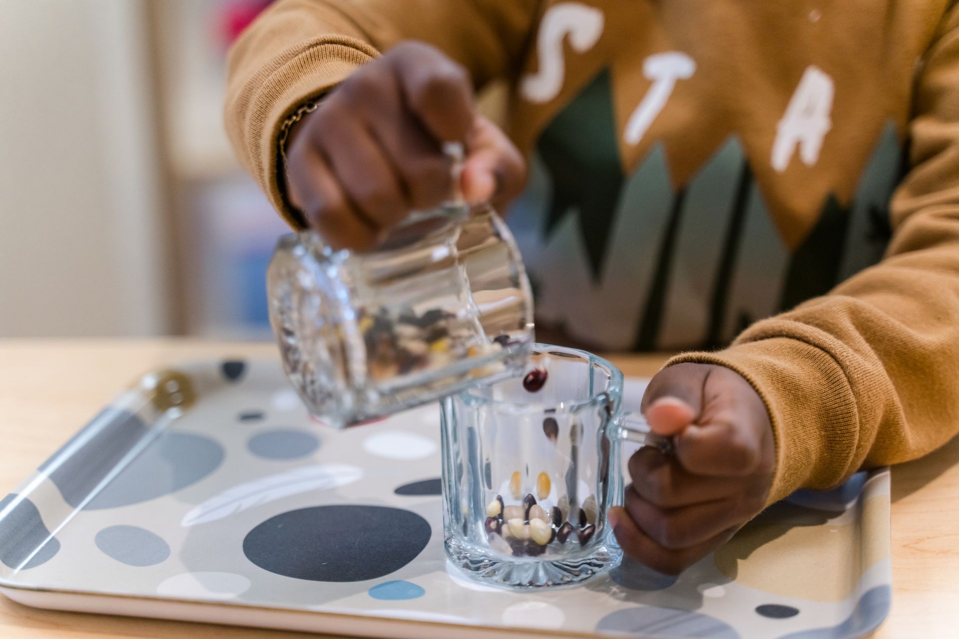 A montessori child is pouring water into a cup on a tray.