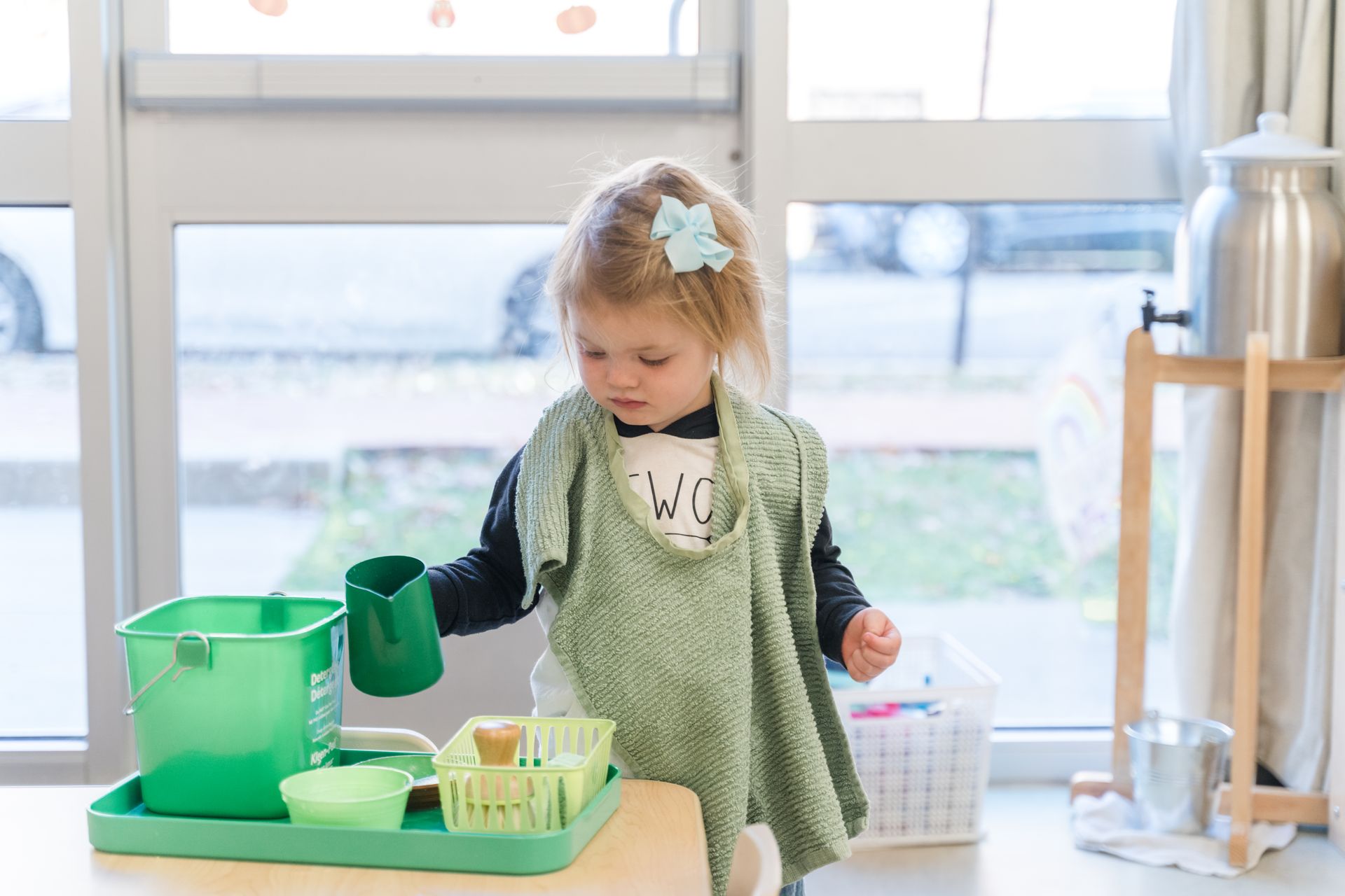 A montessori child is working with a green watering can on a table.