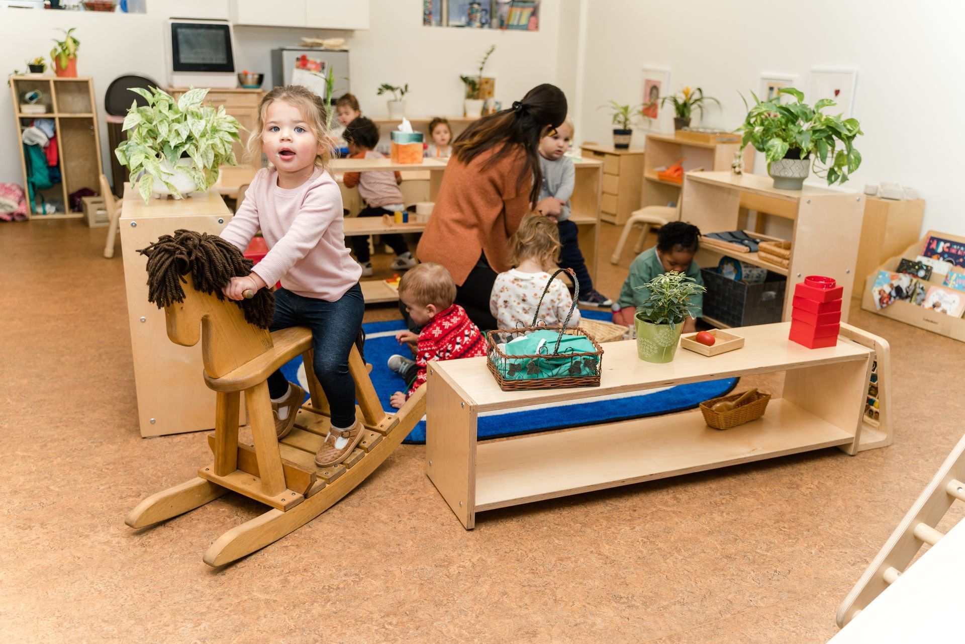 A montessori child is riding a wooden rocking horse in a classroom.