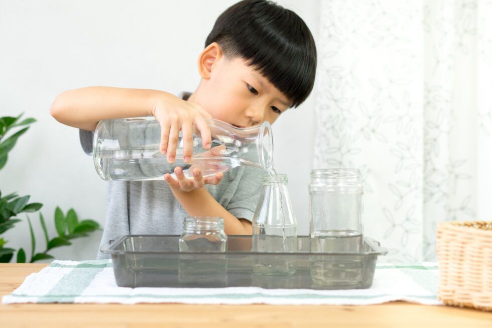 A Montessori child is pouring water into a tray of glasses
