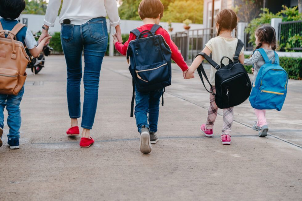 A group of Montessori children with backpacks are walking down a sidewalk holding hands