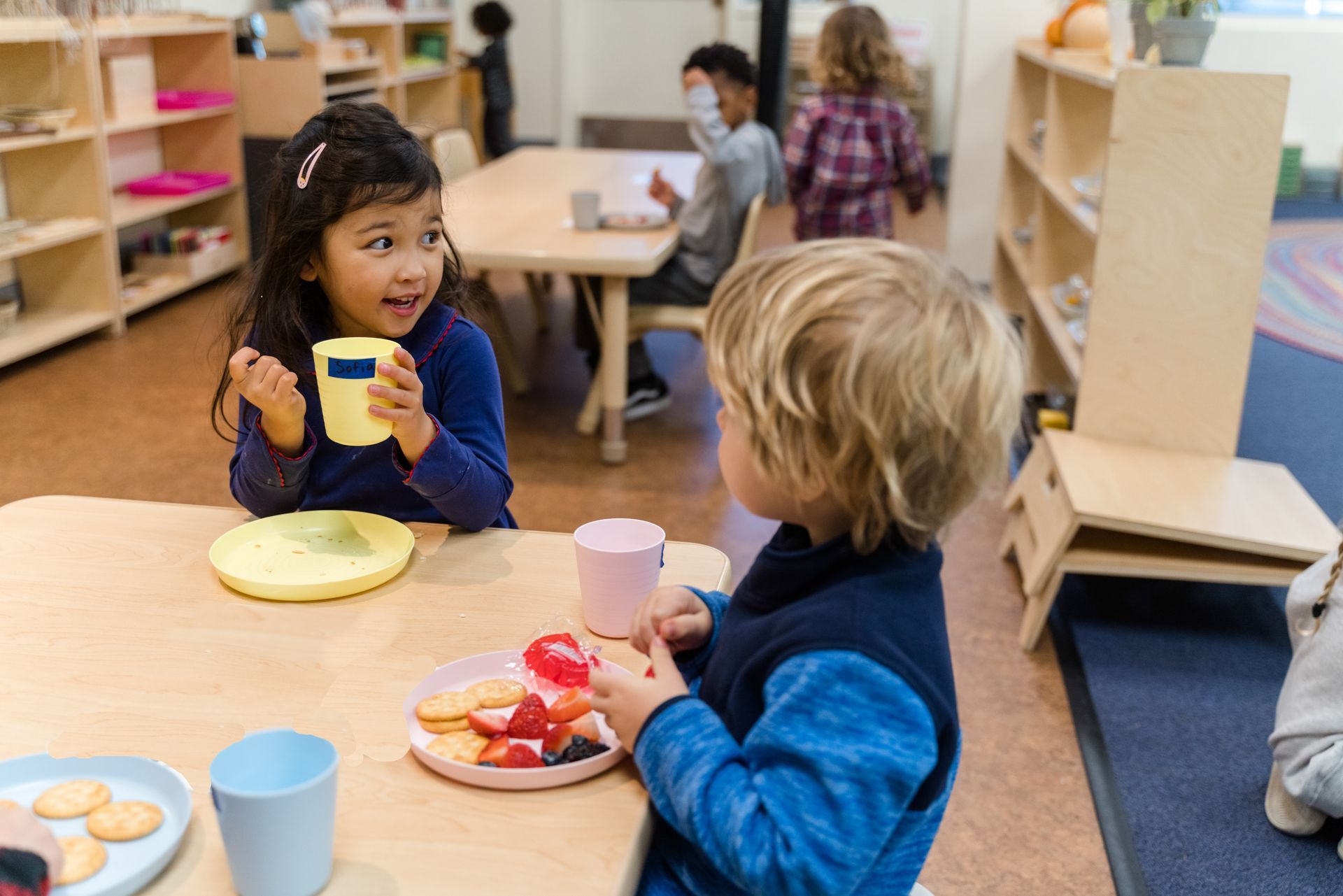 Montessori children are sitting at a table eating food.