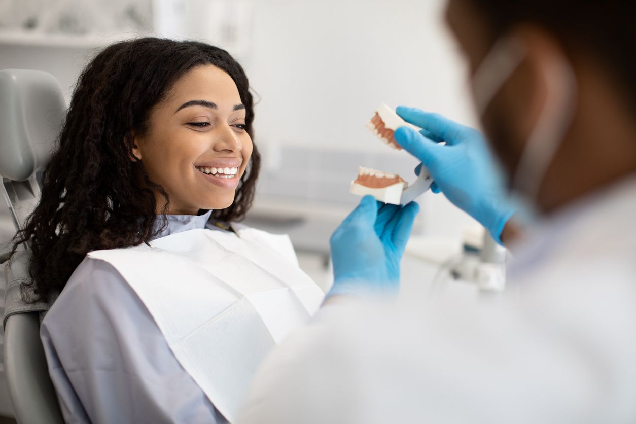 A woman is sitting in a dental chair while a dentist holds a model of her teeth.