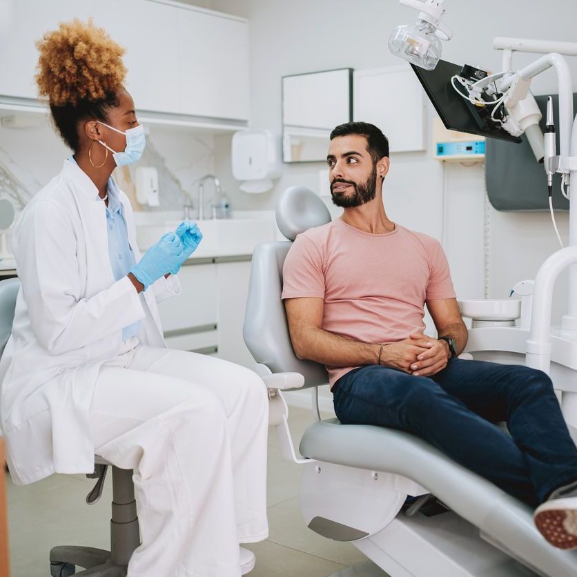 A man is sitting in a dental chair talking to a dentist.