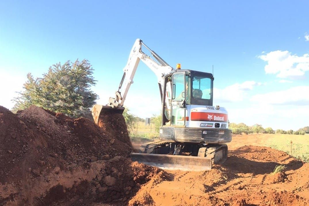 A white and red excavator is digging a hole in the dirt.