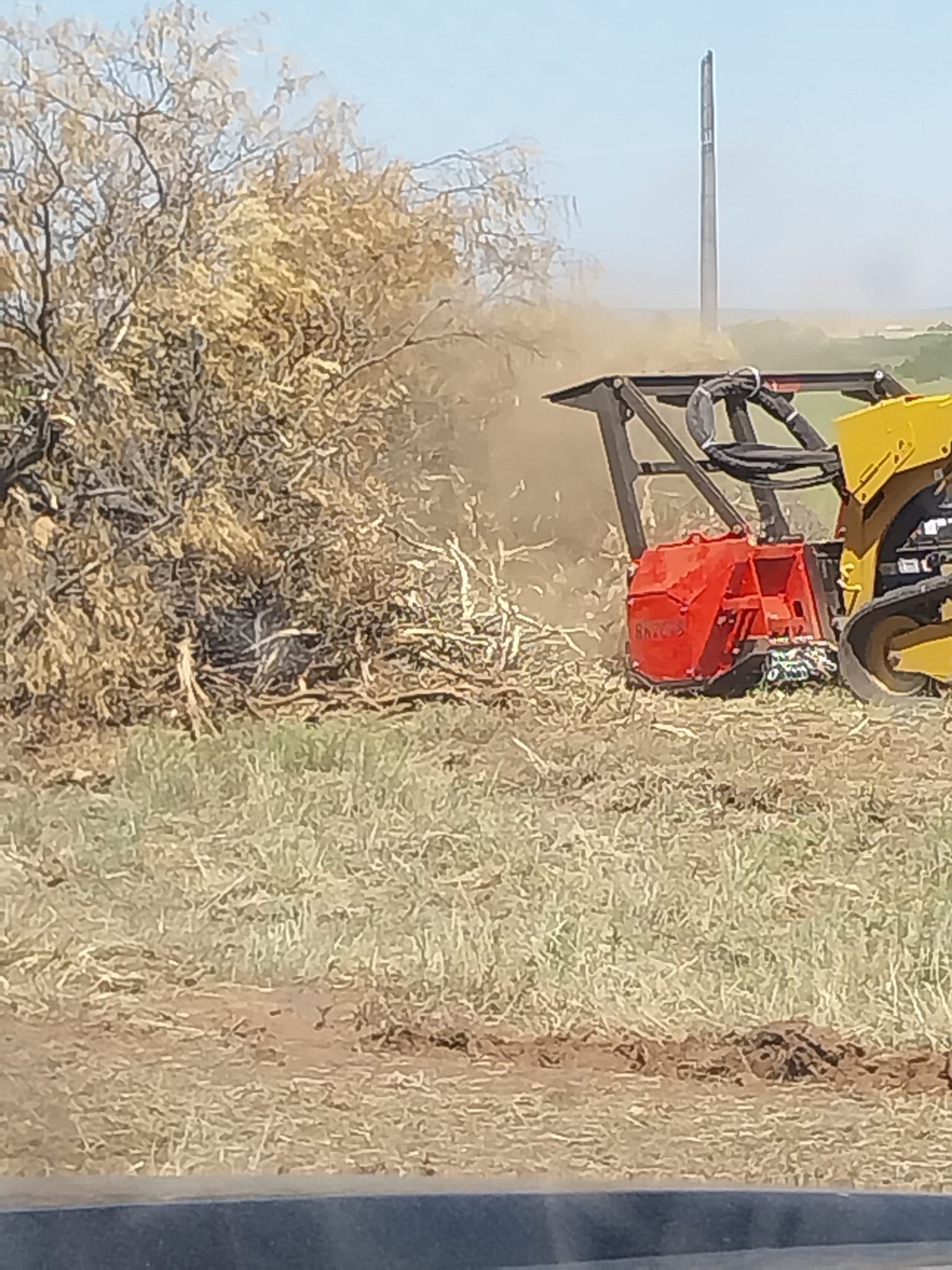 A tractor is cutting a tree stump in a field.