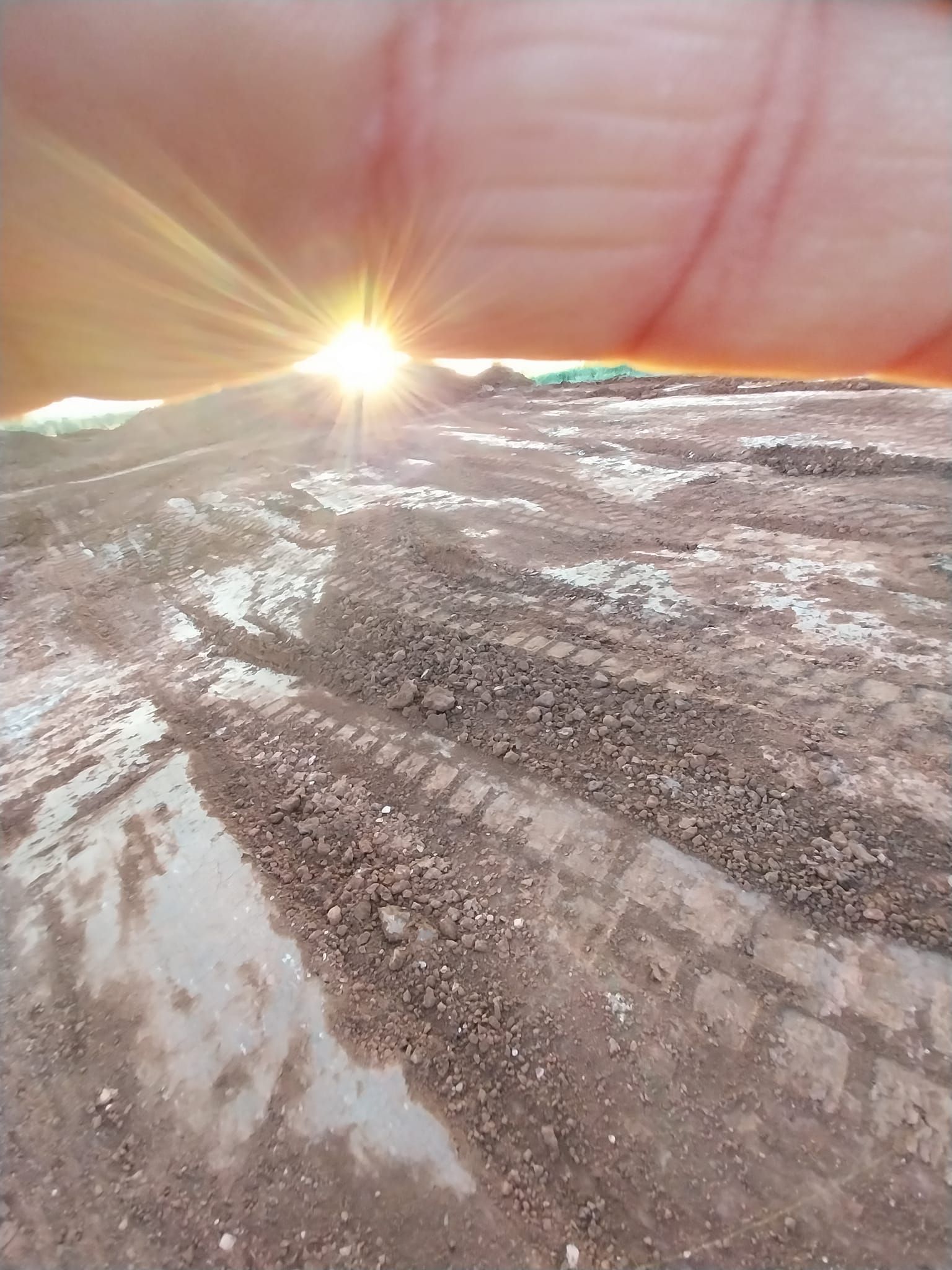 The sun is shining through the clouds over a muddy field.