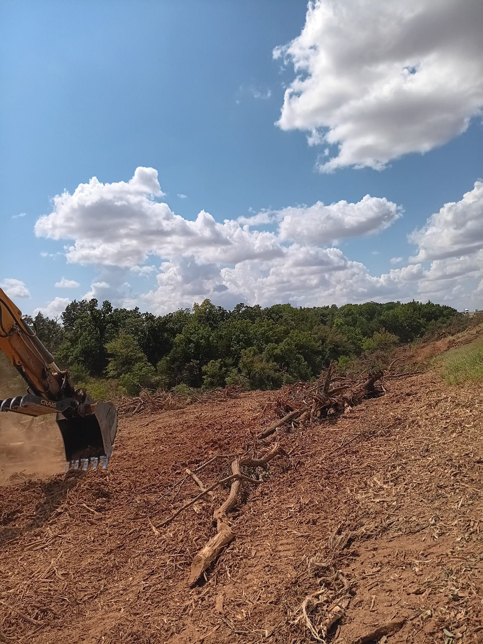 A bulldozer is moving dirt in a field with trees in the background.