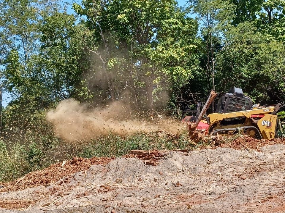 A bulldozer is moving dirt in a field with trees in the background.