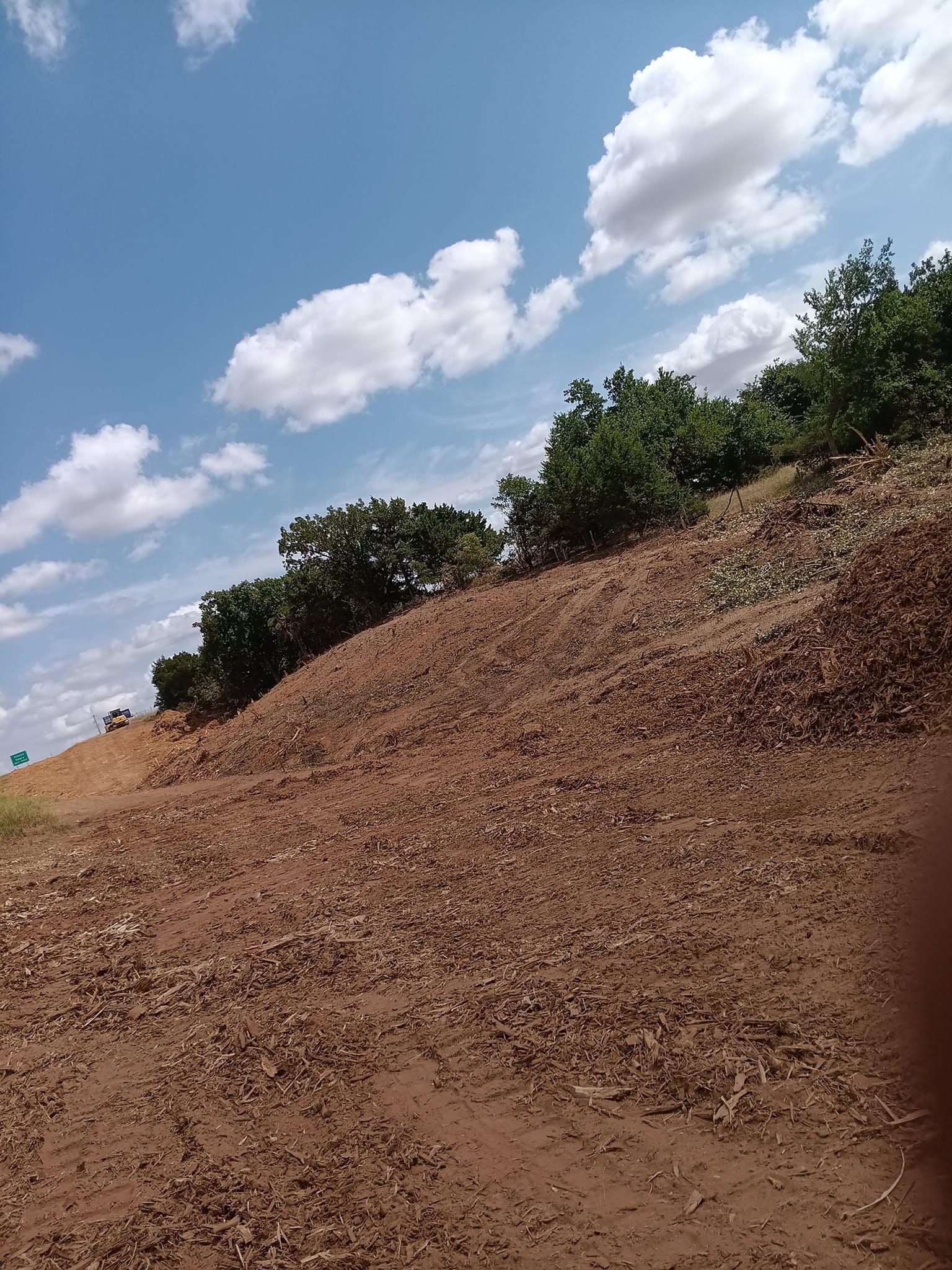 A pile of dirt is sitting on top of a hill with trees in the background.