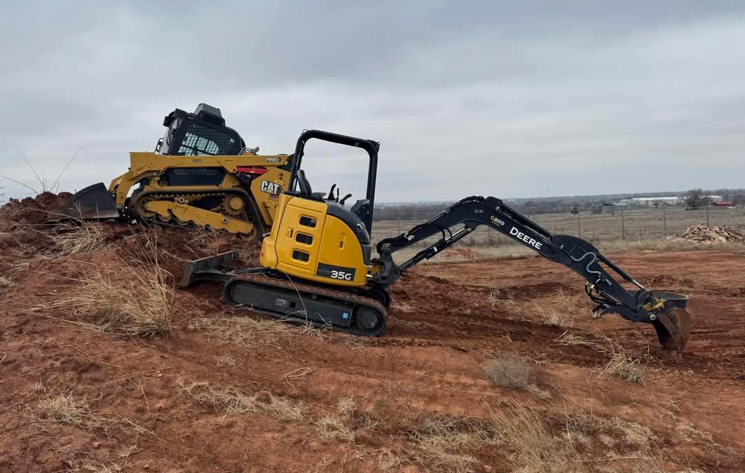 A yellow excavator is digging in a dirt field next to a bulldozer.