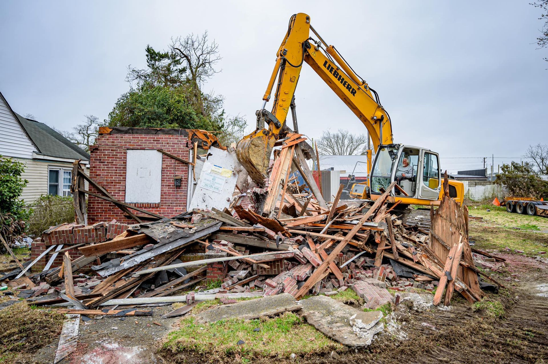 A yellow excavator is demolishing a brick house.