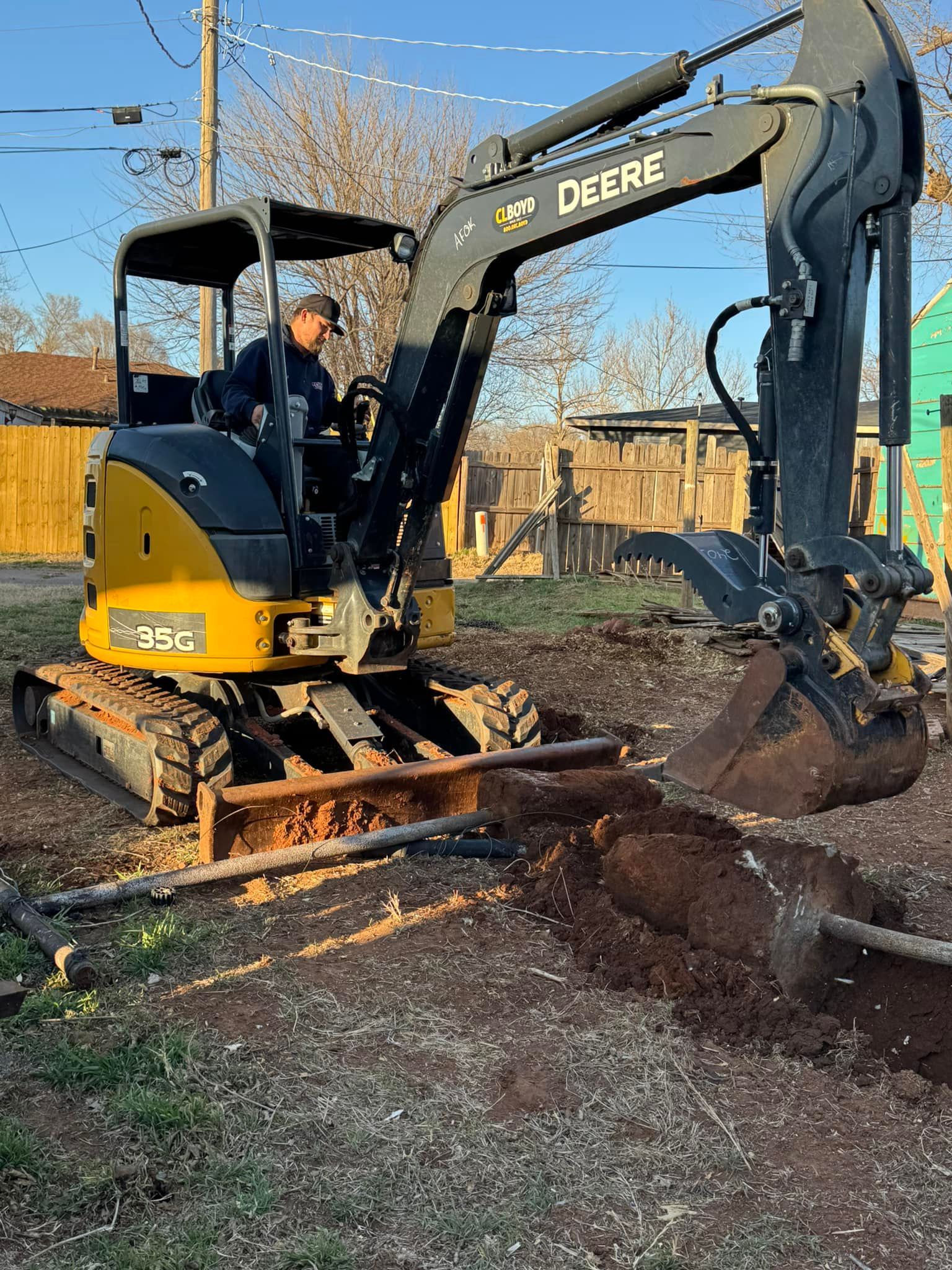 A man is driving a deere excavator in a dirt field.
