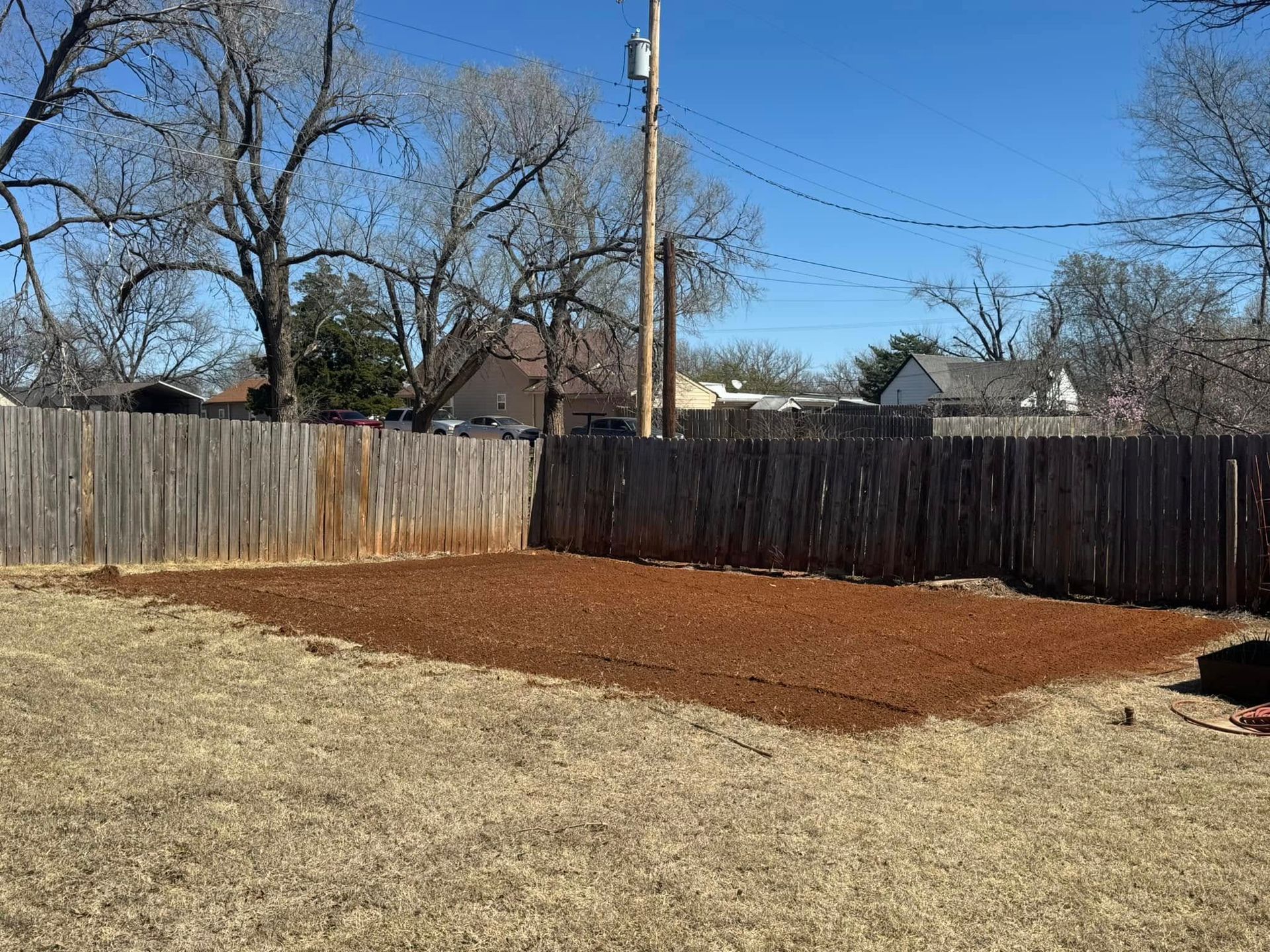 A backyard with a wooden fence and dirt in the middle of it.