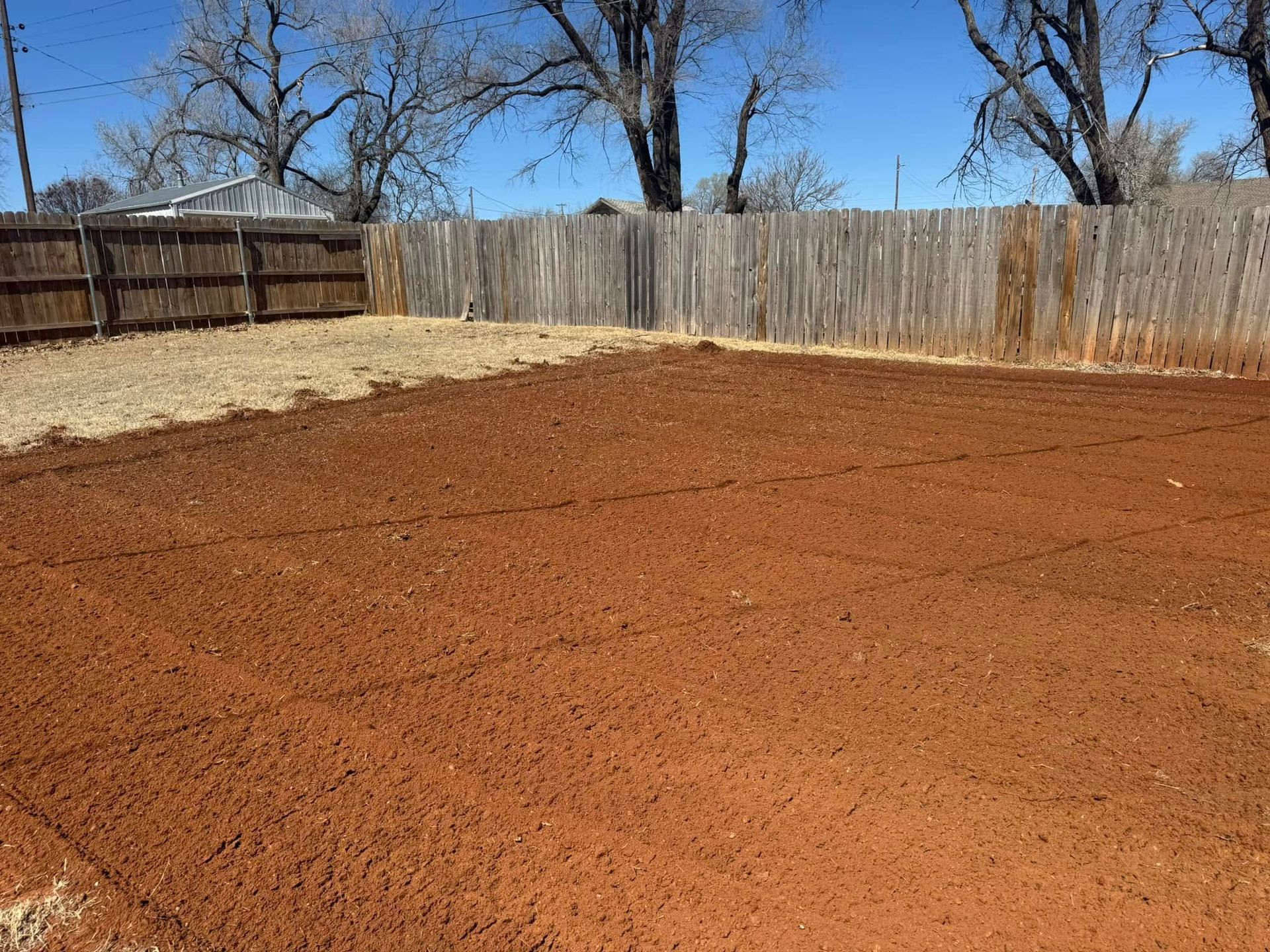 A dirt field with a wooden fence in the background